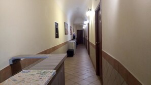 A hotel hallway with a reception desk, framed pictures on the walls, and doors leading to rooms. - Alex Romano (Rome)