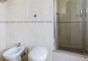 A bathroom with a bidet, toilet, and a glass shower enclosure. - Alex Romano (Rome)