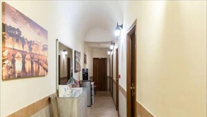 A narrow hallway with a tiled floor, a bench, a counter with a refrigerator, and a door at the end. - Alex Romano (Rome)