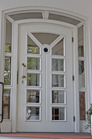 Una entrada blanca con dos puertas y varias ventanas, con un pequeño letrero encima.