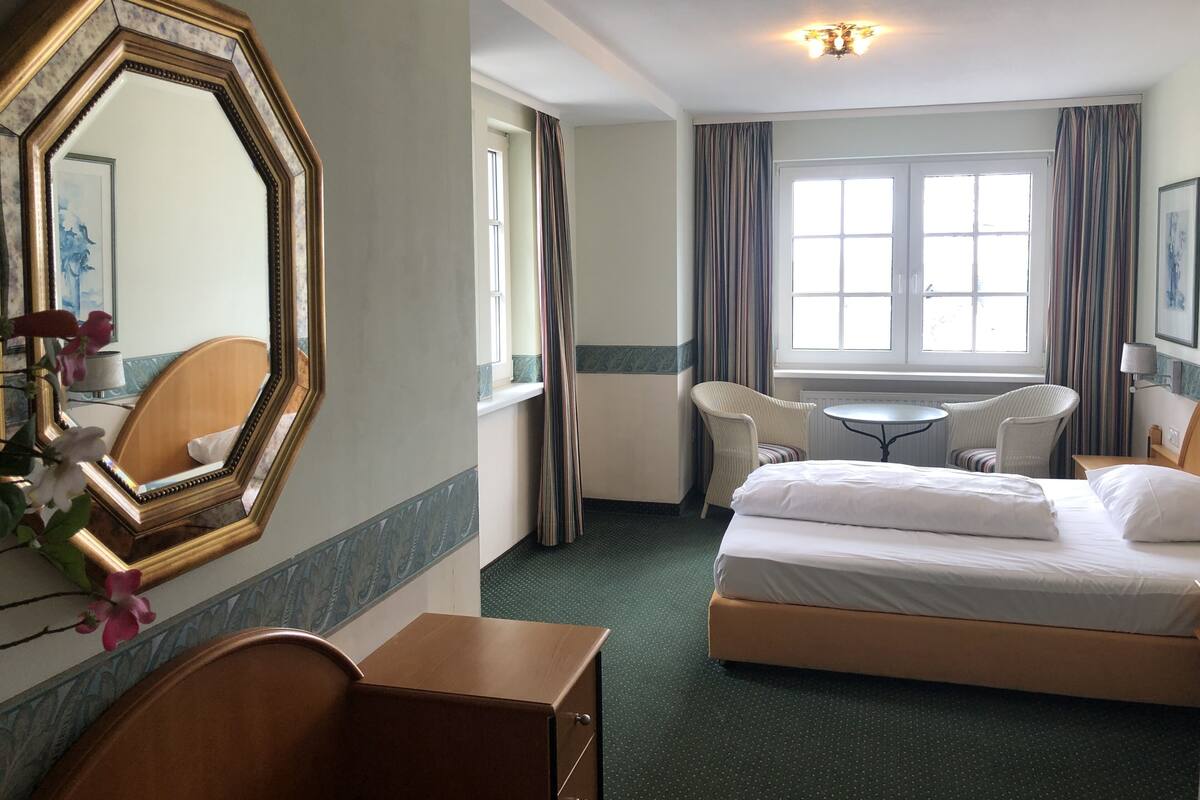 Una habitación de hotel con una cama grande, un escritorio, dos sillas, un espejo y una ventana con cortinas.