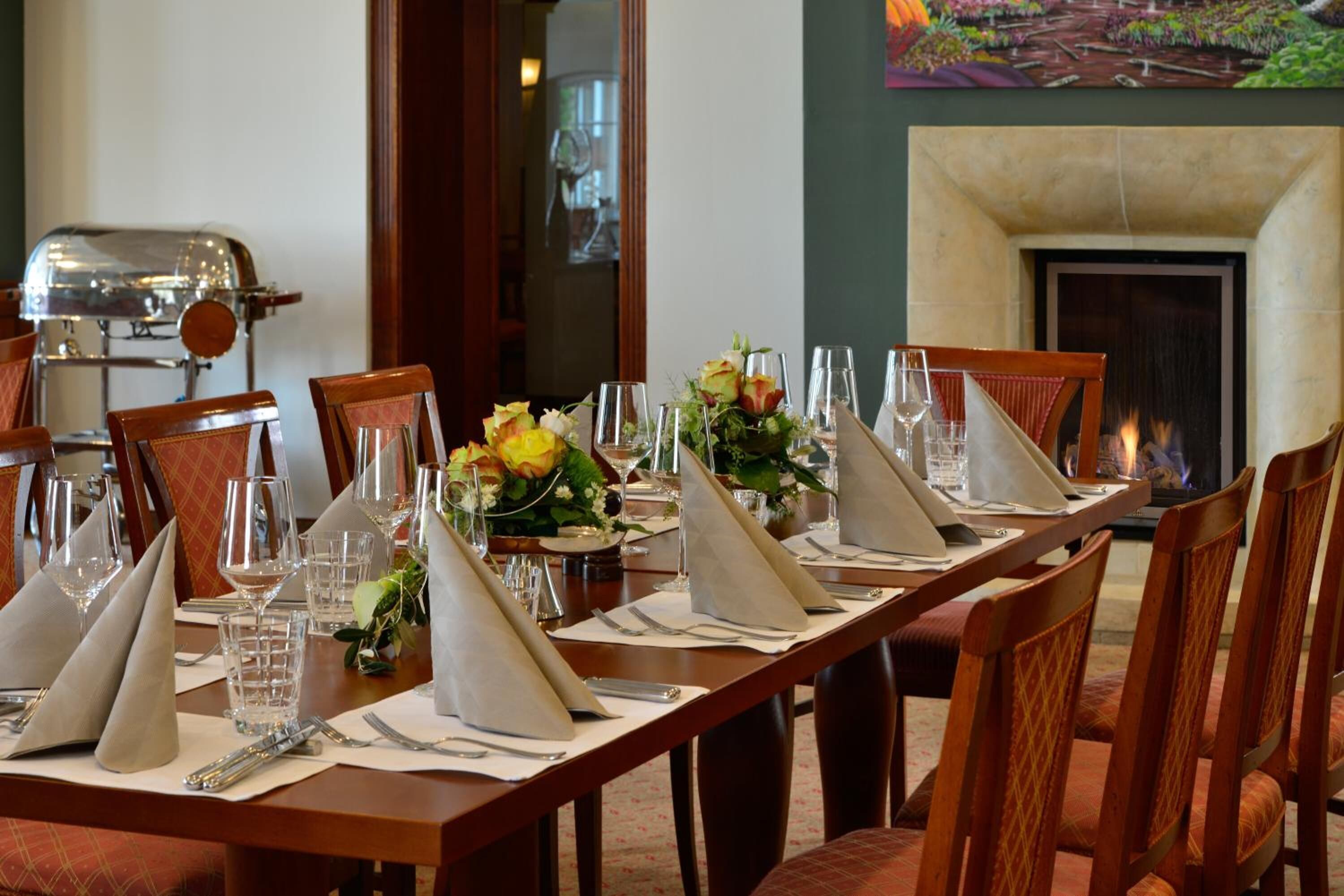 A dining table set for a meal with chairs, a fireplace, and a grill in the background.
