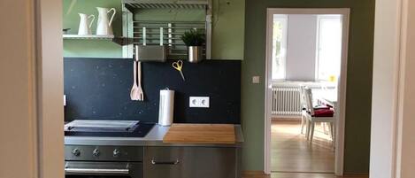 A modern kitchen with stainless steel appliances, a wooden countertop, and a view into a dining area with a red chair.
