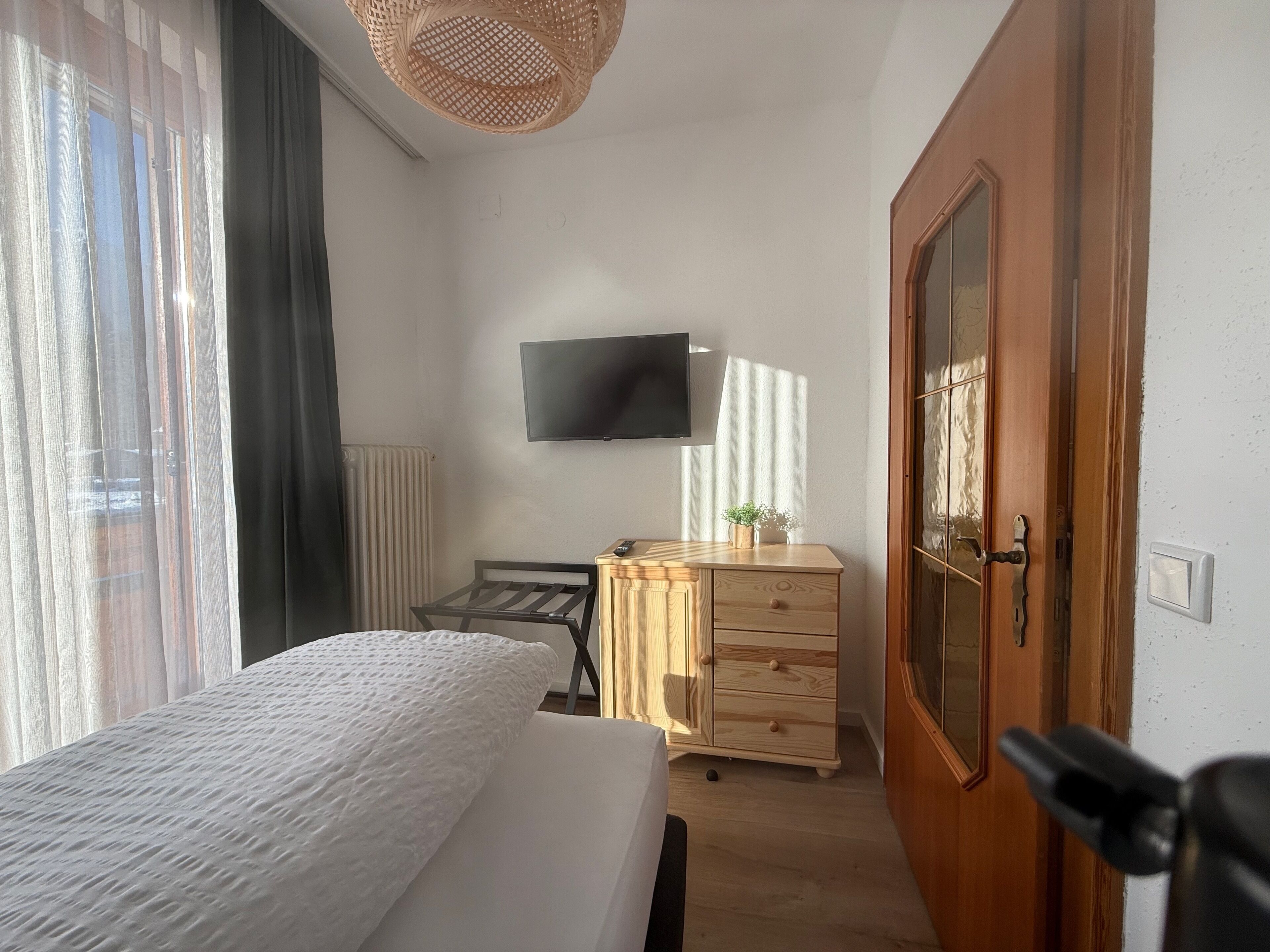 Quarto com cama, cómoda de madeira, televisão e porta.