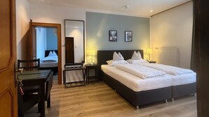A hotel room with a large bed, a desk, and a chair. There is a door leading to another room. - Hotel Berghof (Berg im Drautal)
