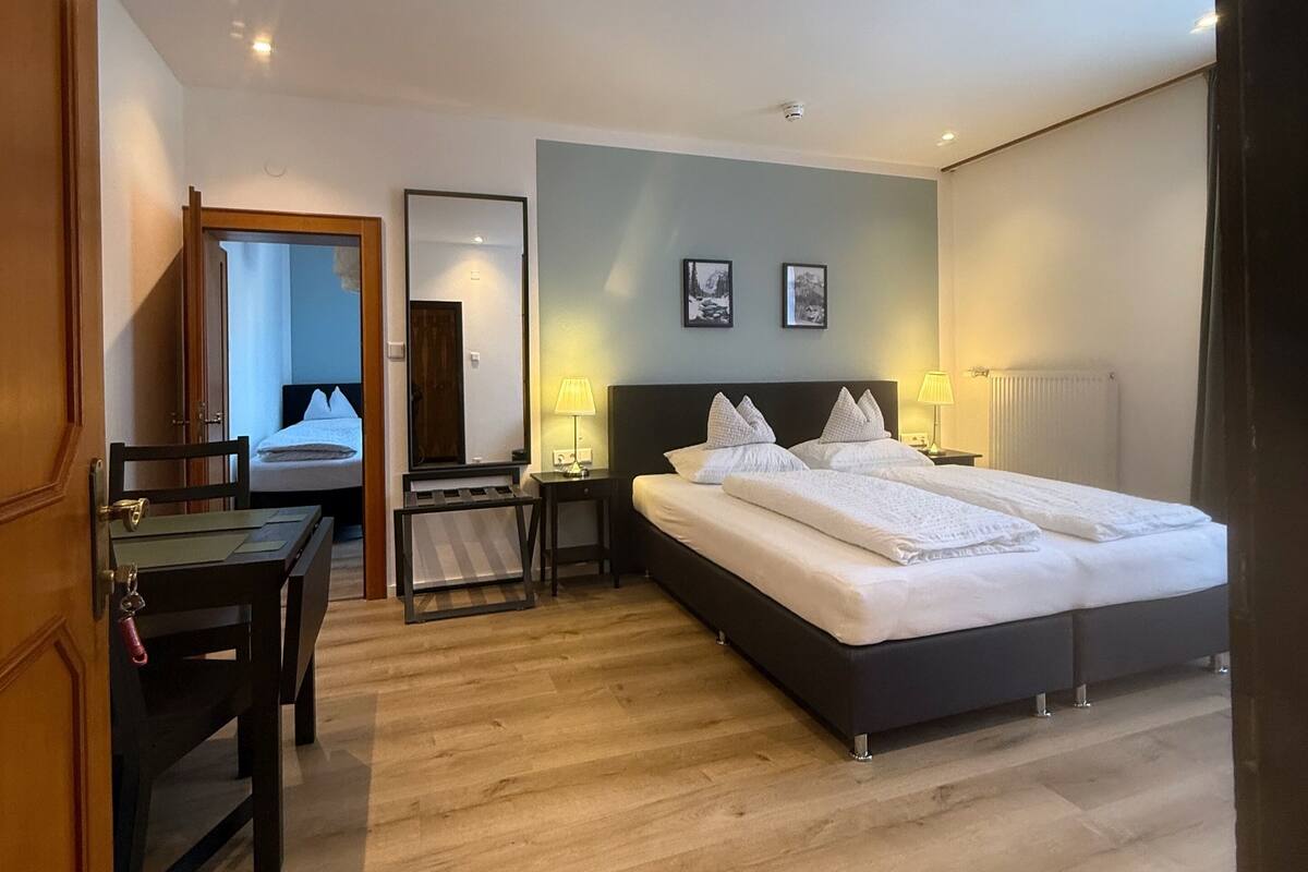 Une chambre d’hôtel avec un grand lit, un bureau et une chaise. Une porte donne accès à une autre pièce.