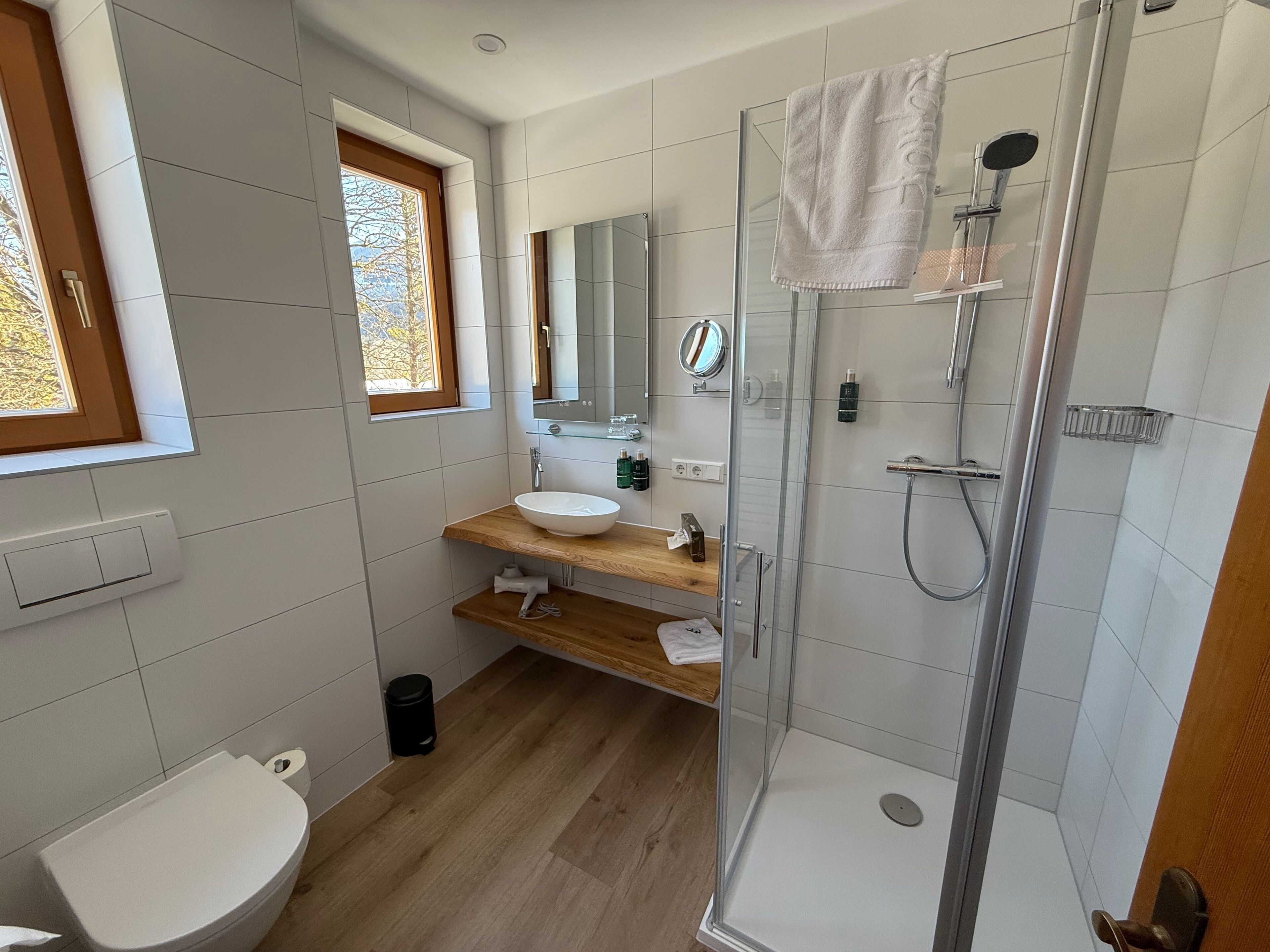 Un baño moderno con ducha acristalada, tocador de madera, lavabo blanco y un inodoro.