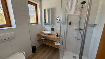 Un baño moderno con ducha acristalada, tocador de madera, lavabo blanco y un inodoro.