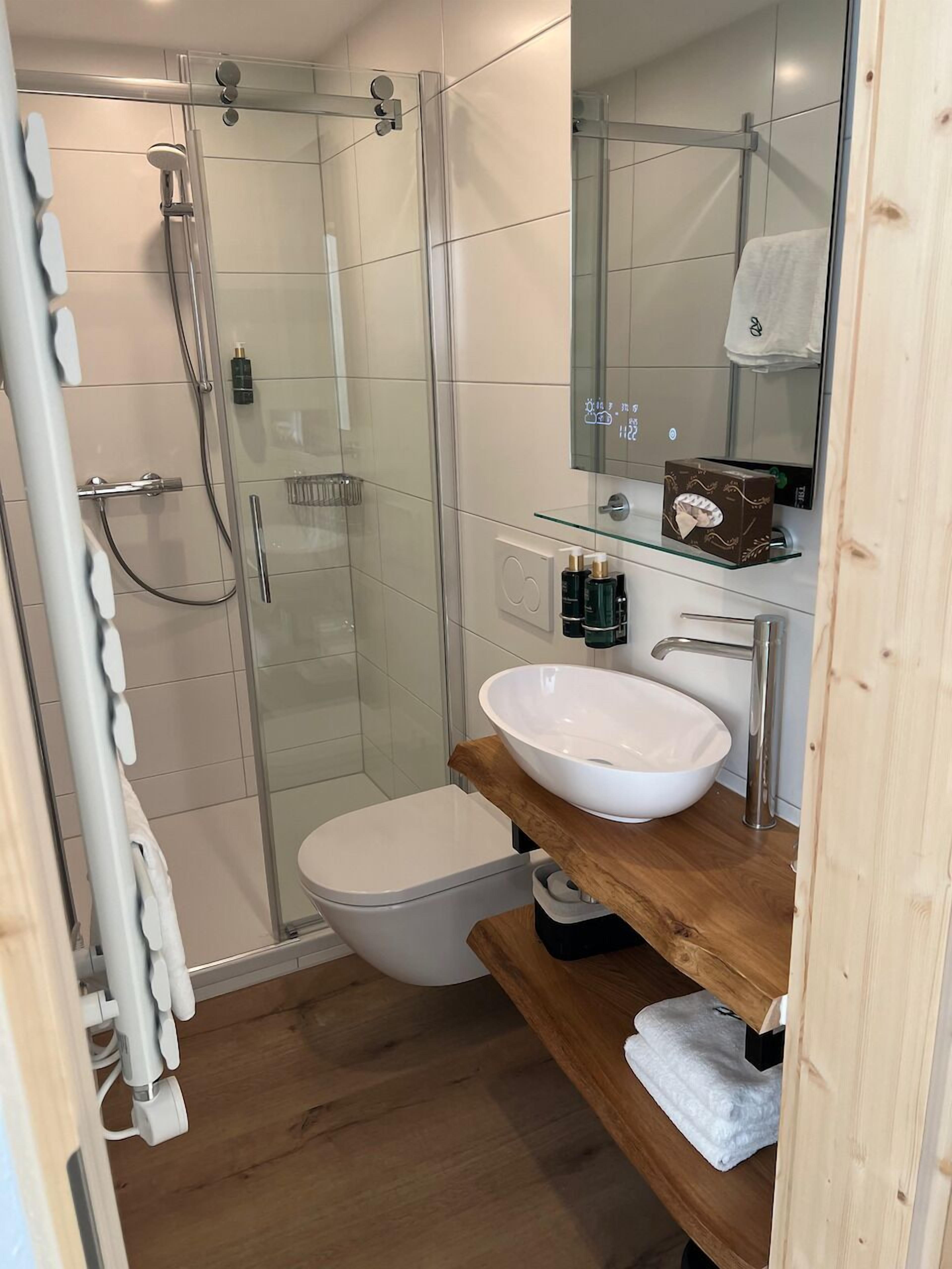 A modern bathroom with a glass-enclosed shower, a white toilet, and a wooden vanity with a white sink.