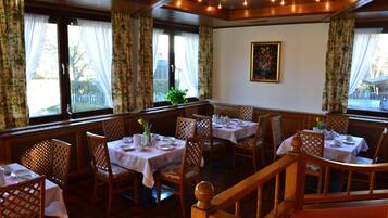 Comedor con mesas dispuestas para cuatro personas, sillas de madera y una escalera que sube a un nivel superior.