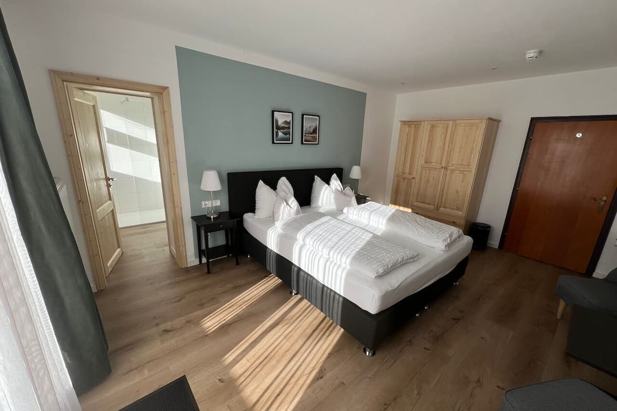 Une chambre avec un grand lit, un plancher en bois, une armoire et une porte.