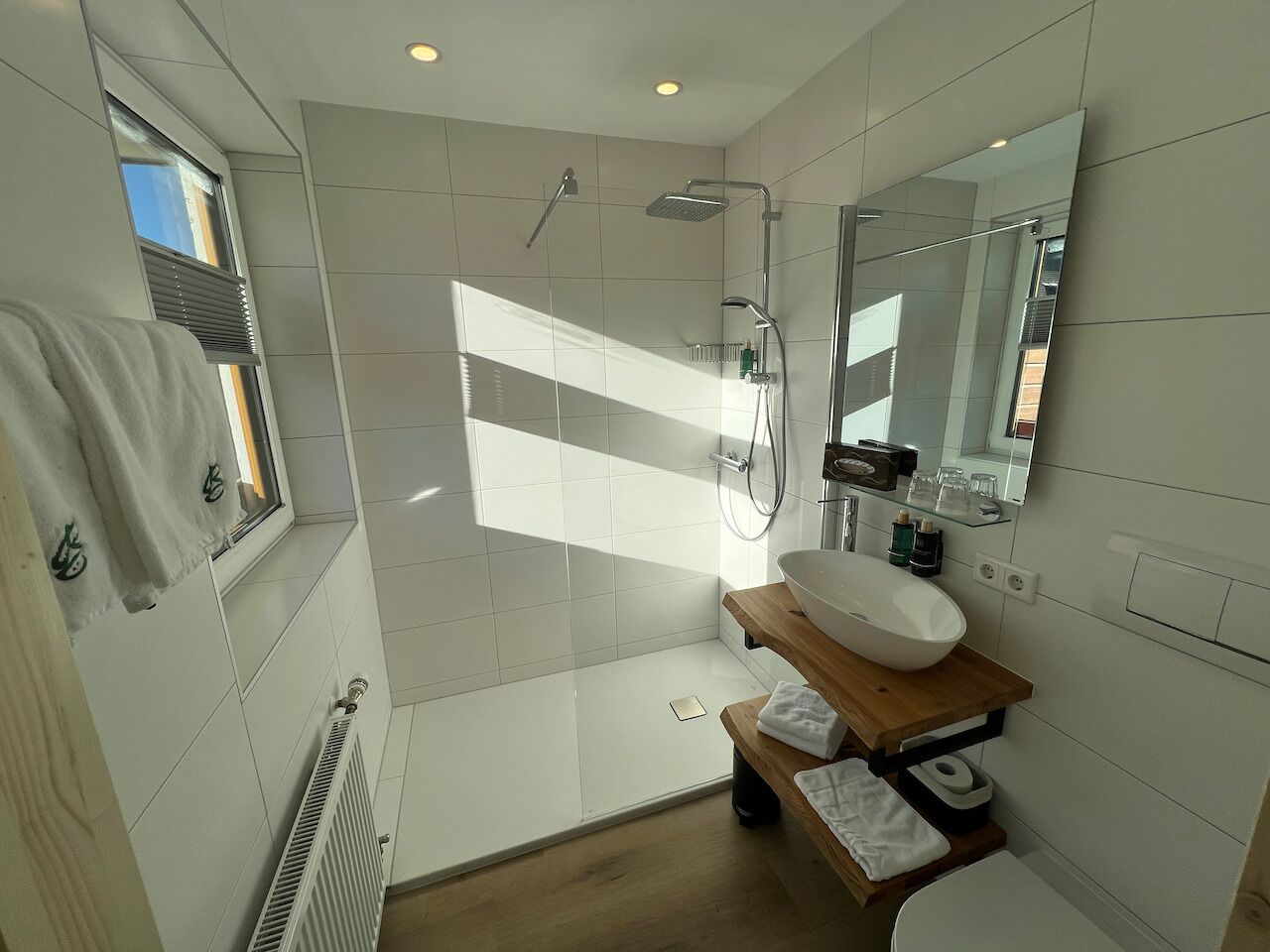 Ein modernes Badezimmer mit einem großen Spiegel, einer Holzwaschgelegenheit, einem weißen Waschbecken und einer Duschkabine.