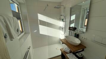 Uma casa de banho moderna com um espelho grande, toucador de madeira, lavatório branco e zona de duche.