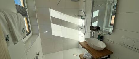 A modern bathroom with a large mirror, a wooden vanity, a white sink, and a shower area.