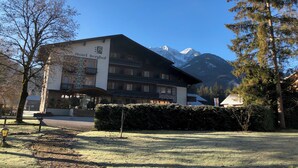 A hotel with a mountain backdrop, featuring a traditional Alpine architectural style, a well-maintained lawn, and a clear sky. - Hotel Berghof (Berg im Drautal)