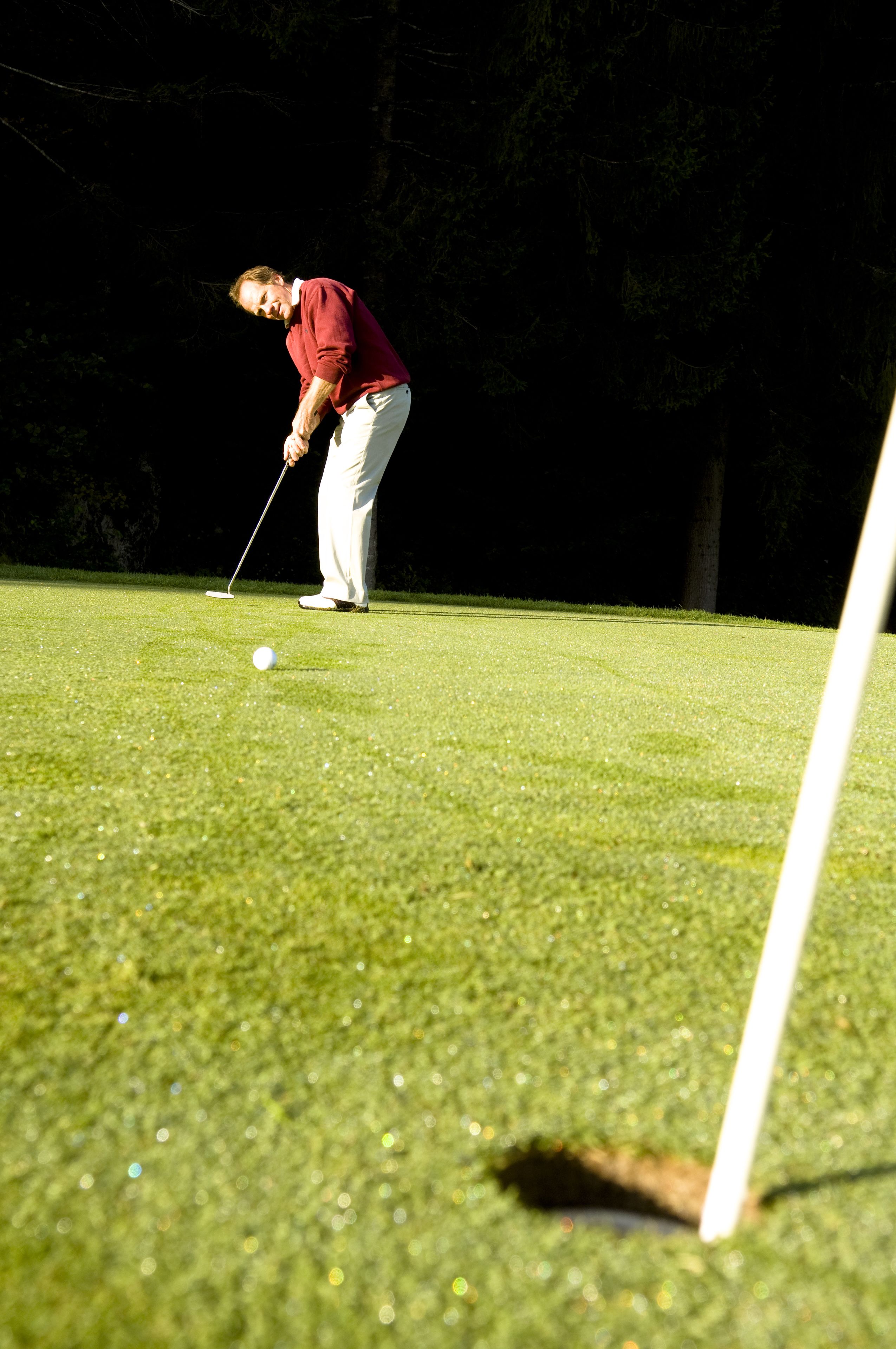 Een golfbaan met een putting green, een golfbal en een golfer in een rood shirt en witte broek die zich klaarmaakt om te putten.