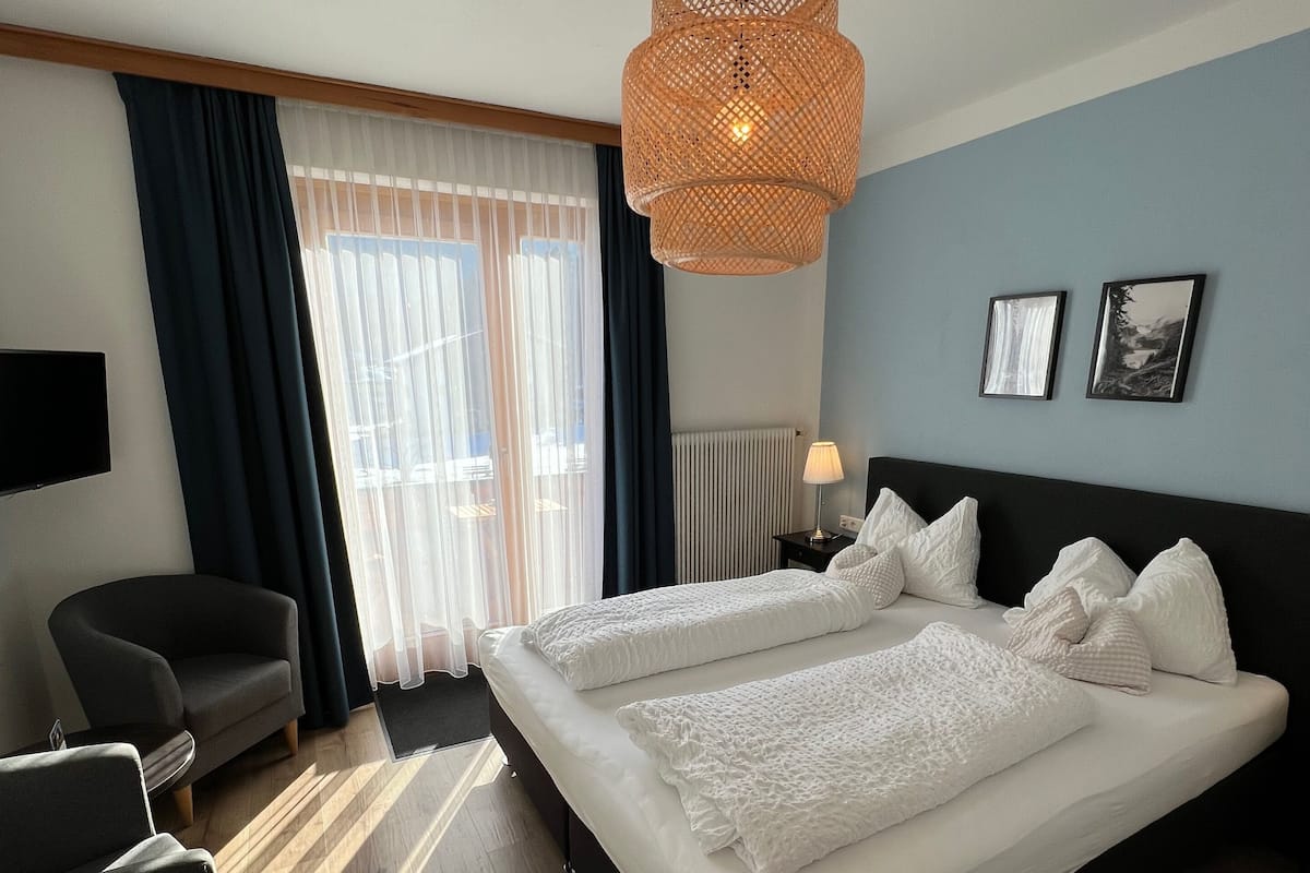 Une chambre d’hôtel avec un grand lit, une chaise, une télévision et une fenêtre avec des rideaux.