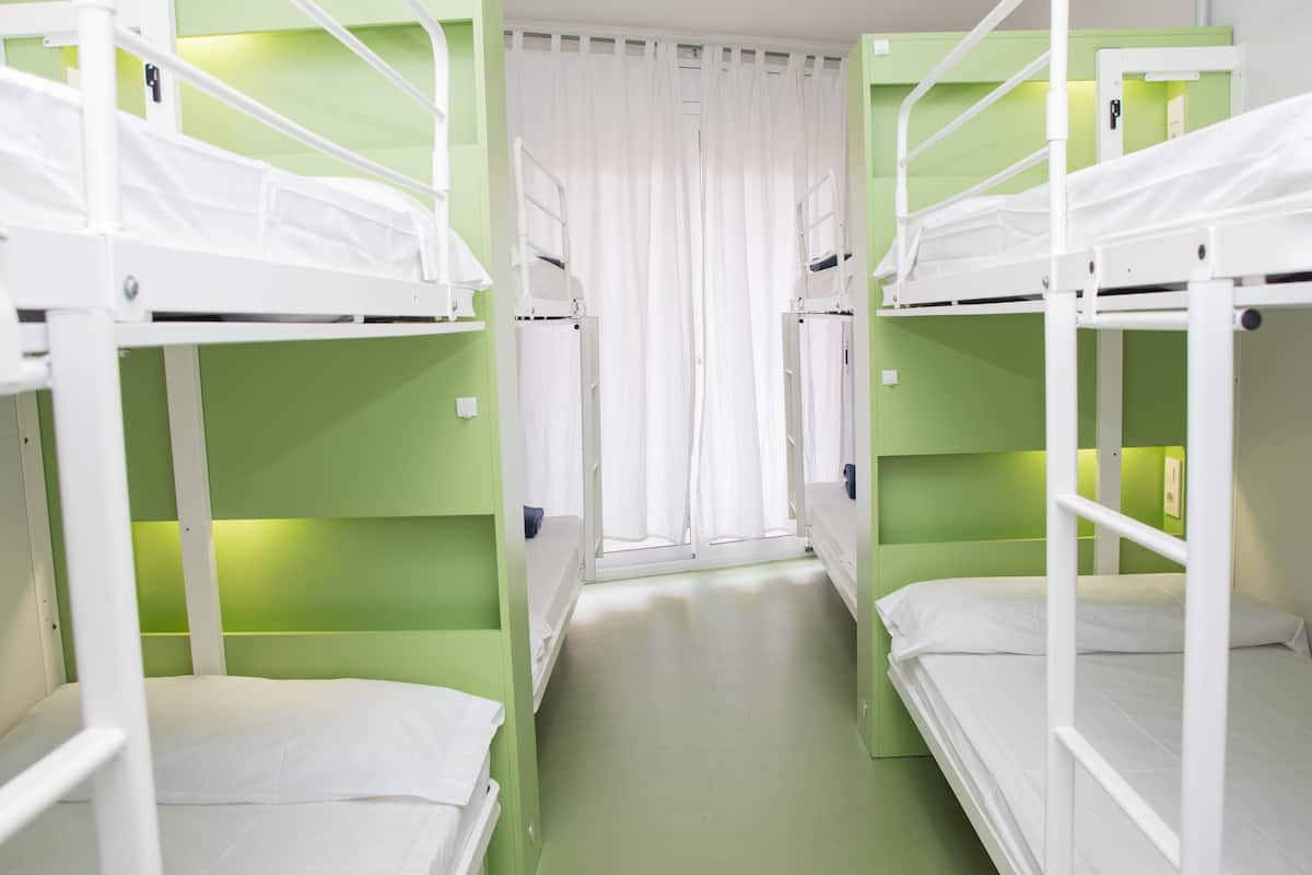 A room with bunk beds, a window with curtains, and green walls.