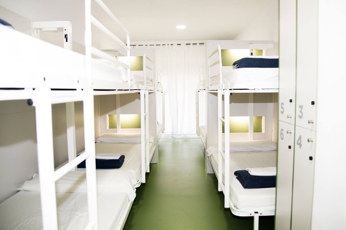 A corridor with bunk beds and lockers, indicating a dormitory-style accommodation.