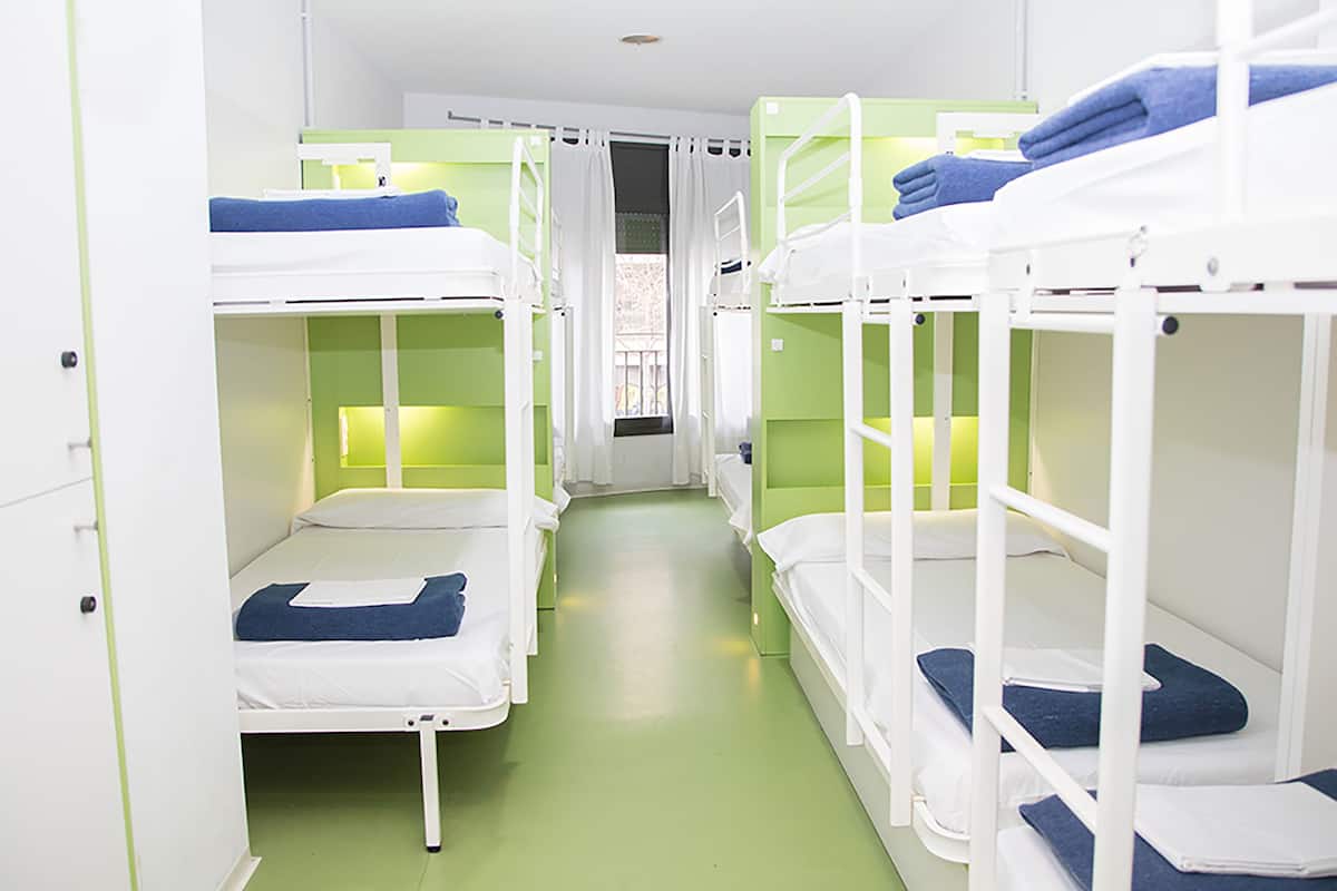 A corridor with bunk beds, green walls, and a window with curtains.