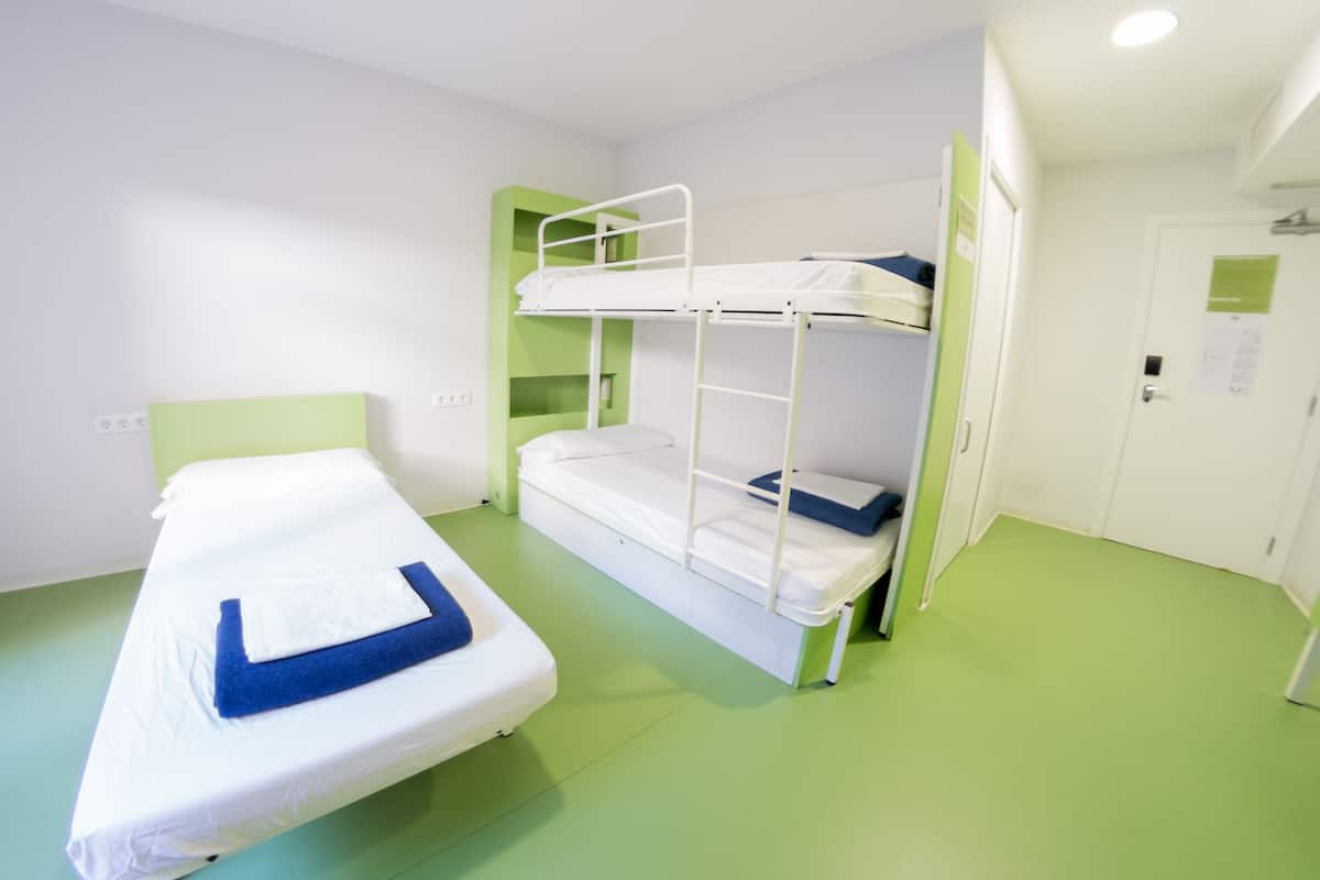 A bunk bed room with a single bed and a bunk bed. The room has green walls and a green floor. There is a white door and a white wall with a white switchboard.