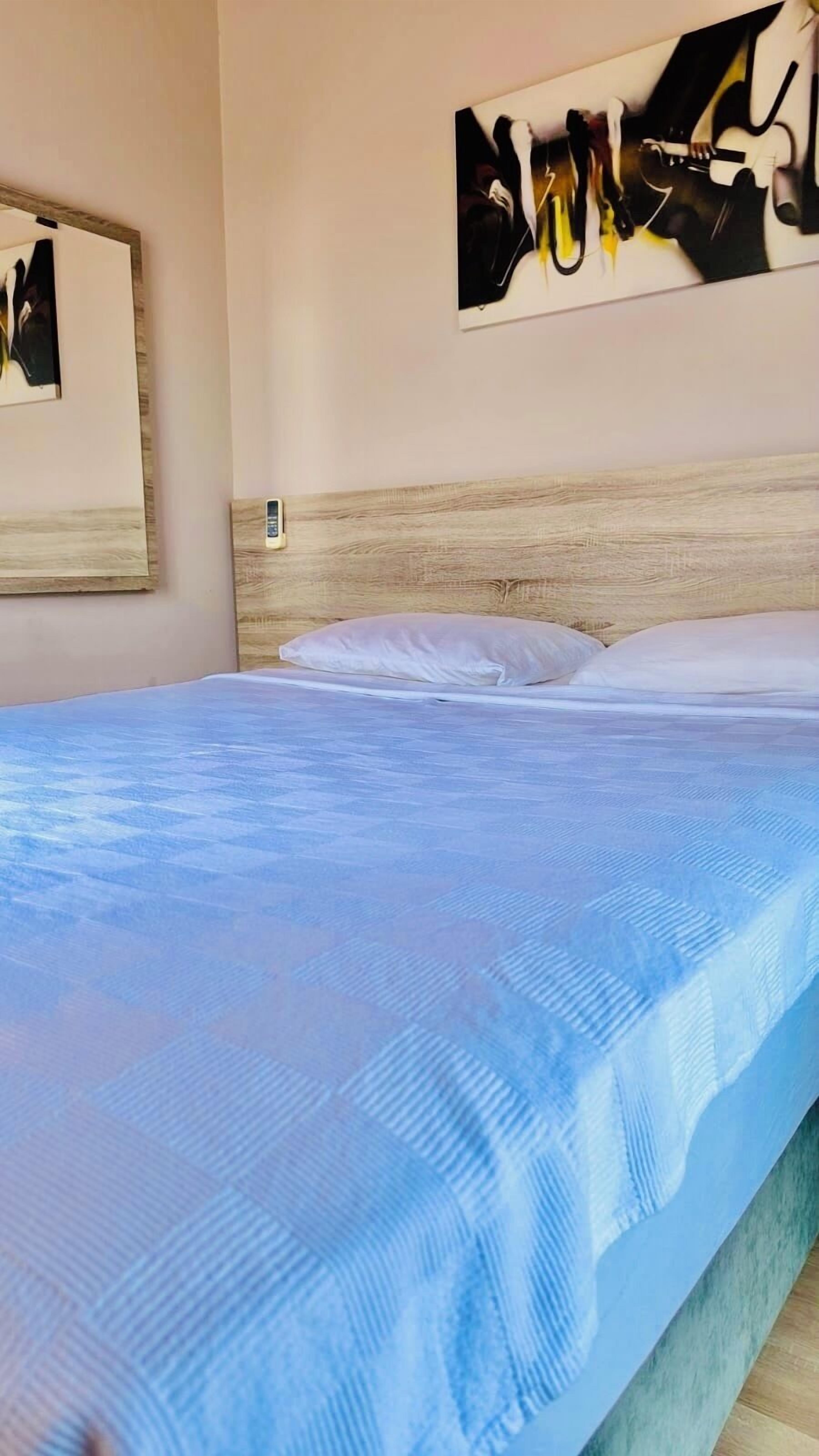 A bedroom with a bed, pillows, a wooden headboard, and a wall-mounted artwork.