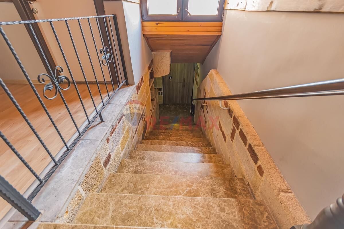 Una escalera con barandilla de metal, escalones de madera y vista a una habitación con ventana y puerta.