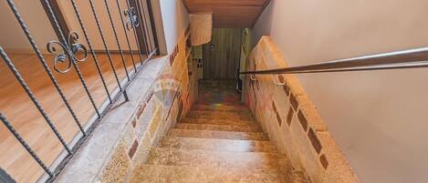Una escalera con barandilla de metal, escalones de madera y vista a una habitación con ventana y puerta.