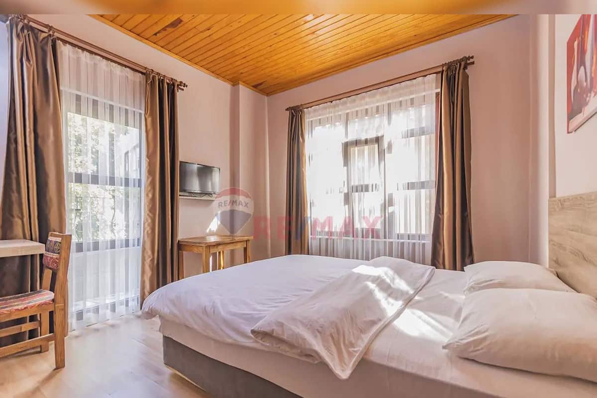 A bedroom with a bed, a TV on a stand, and a window with curtains.