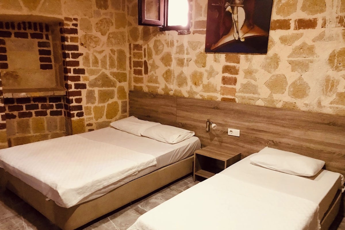 A room with two single beds, a wooden headboard, a stone wall, and a small wooden nightstand.