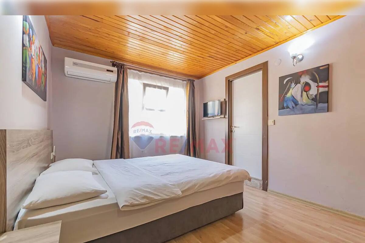 A bedroom with a wooden ceiling, a bed with white bedding, a TV on the wall, and a painting.