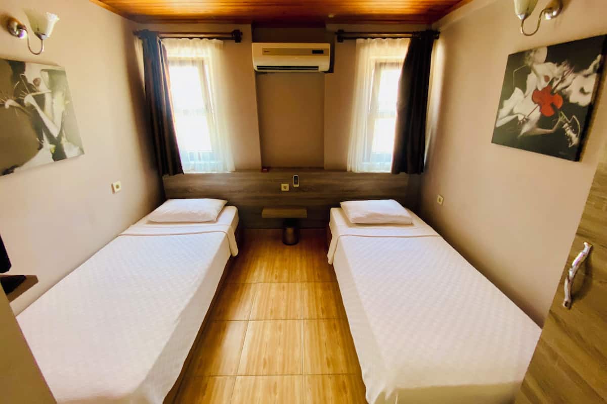 A room with two single beds, wooden flooring, an air conditioning unit, and a painting on the wall.