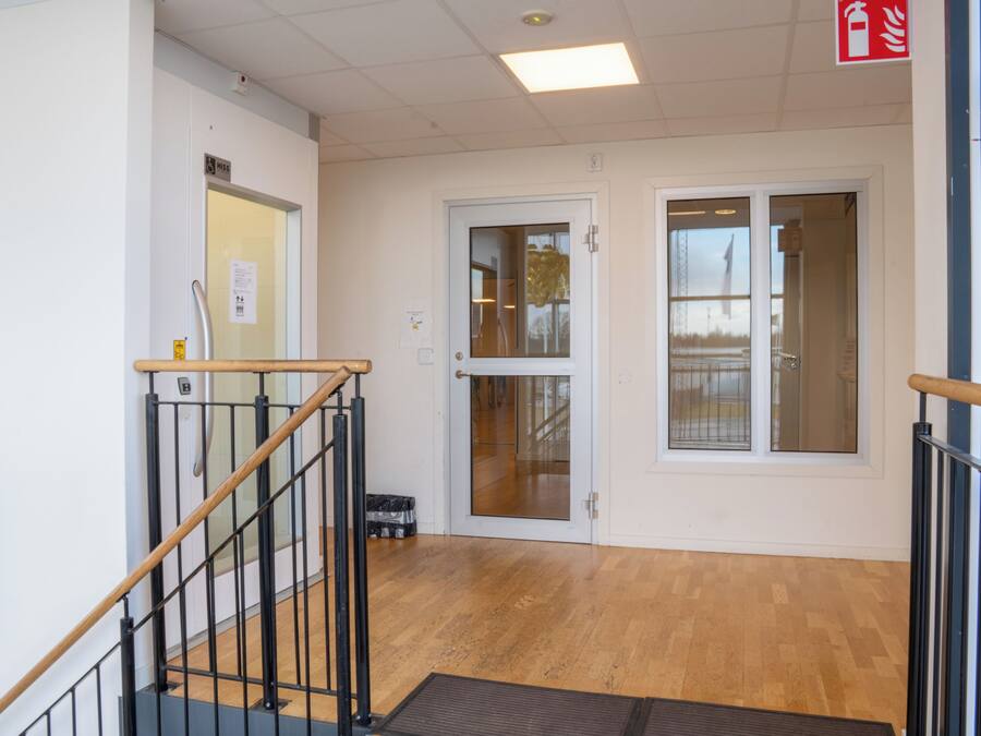 Een trap met een houten leuning en zwarte metalen balustrades, die leidt naar een kamer met een houten vloer en een deur met een ruit.