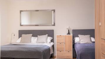A bedroom with two beds, a wardrobe, a mirror, and a bedside lamp.