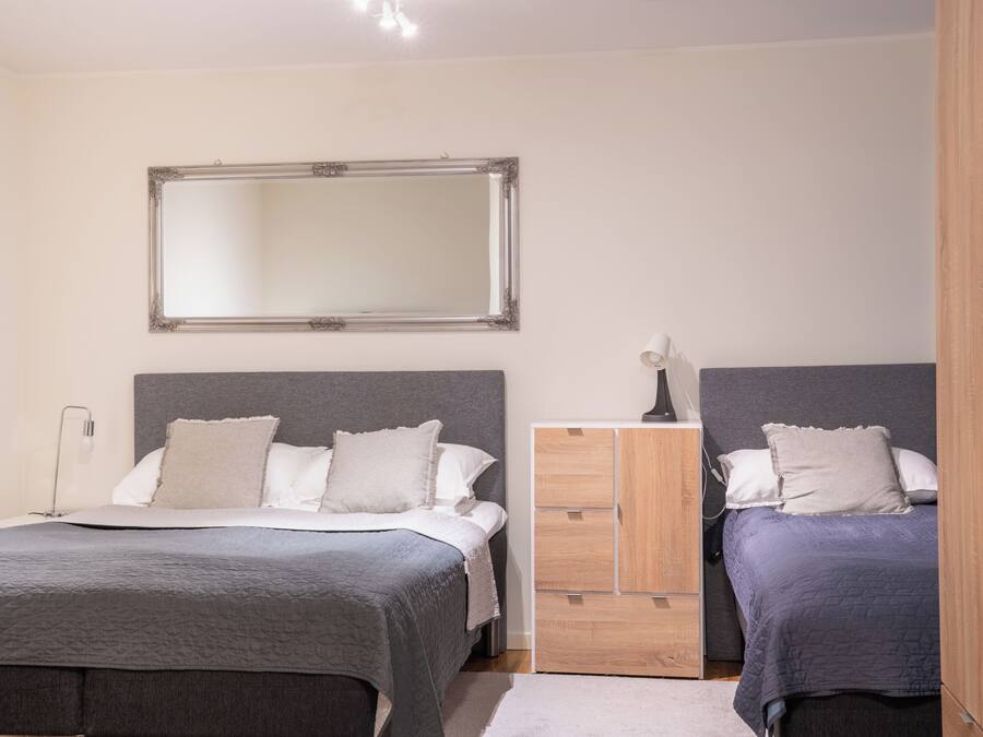 A bedroom with two beds, a wardrobe, a mirror, and a bedside lamp.