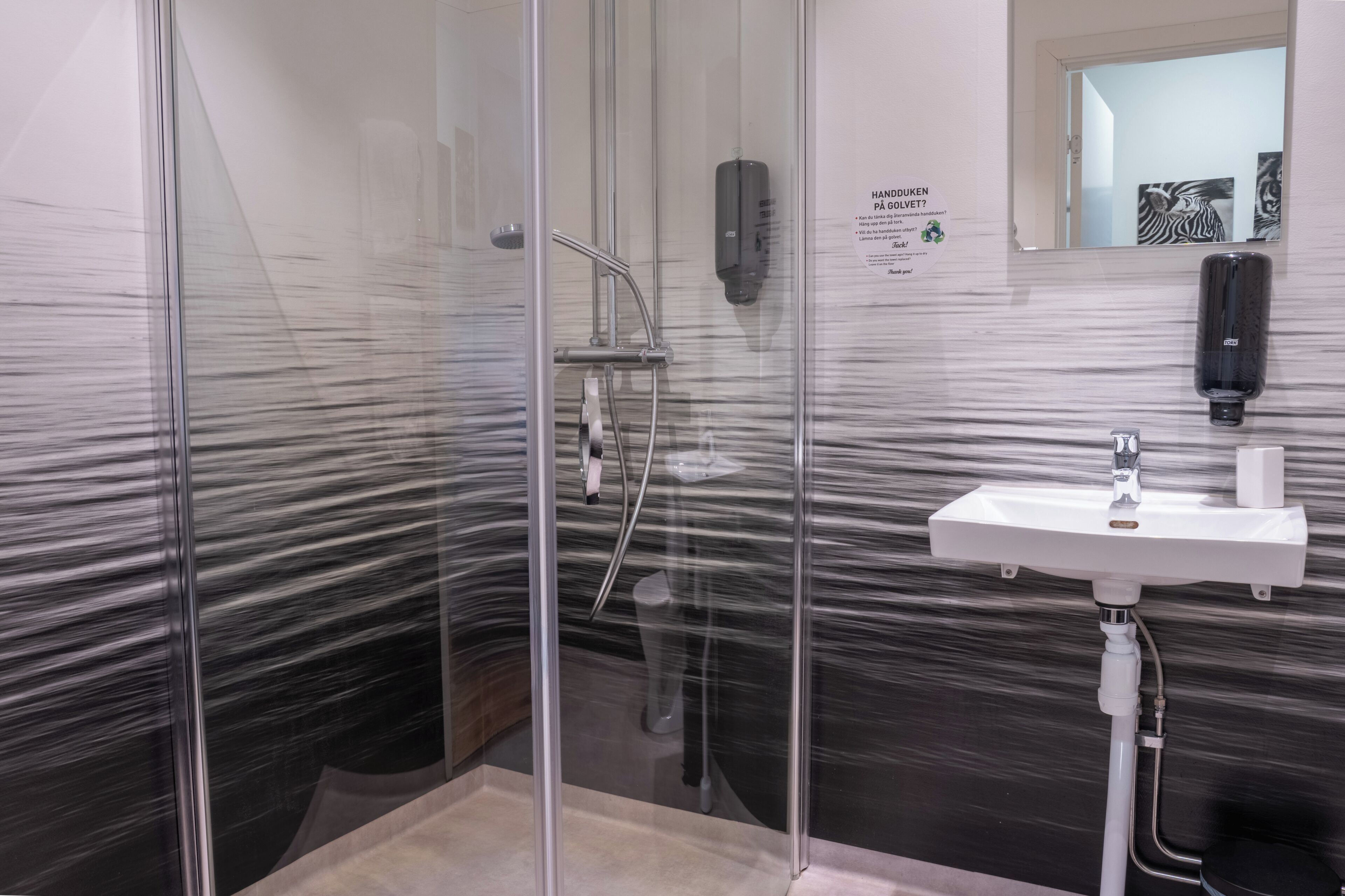 Een moderne badkamer met een glazen douchecabine, een witte wastafel en een spiegel.