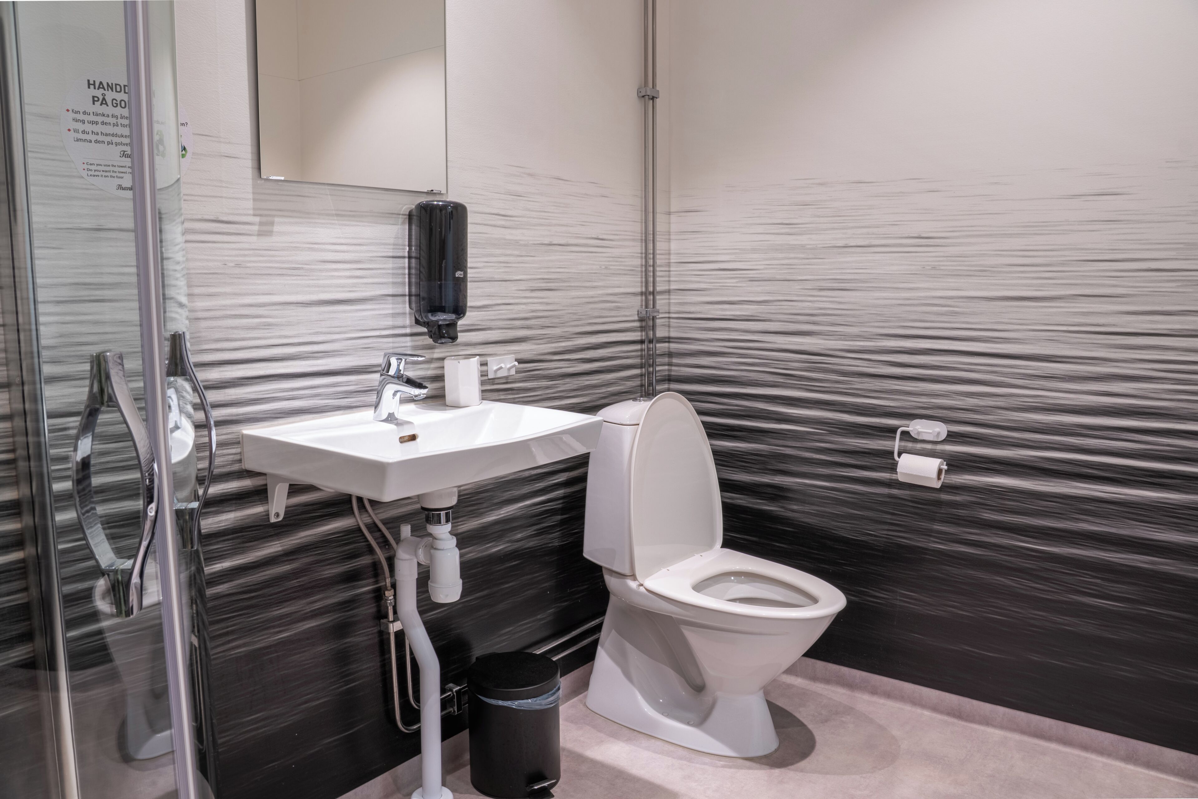 Un bagno moderno con una parete in marmo, un lavabo bianco, un water, un asciugamani ad aria e un cestino.