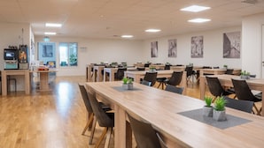 A spacious dining area with long wooden tables, black chairs, and potted plants. - Hotell Tunapark (Eskilstuna)