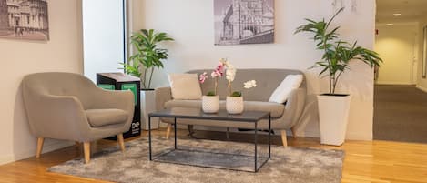 A room with a sofa, armchair, coffee table, potted plants, and two framed pictures on the wall.