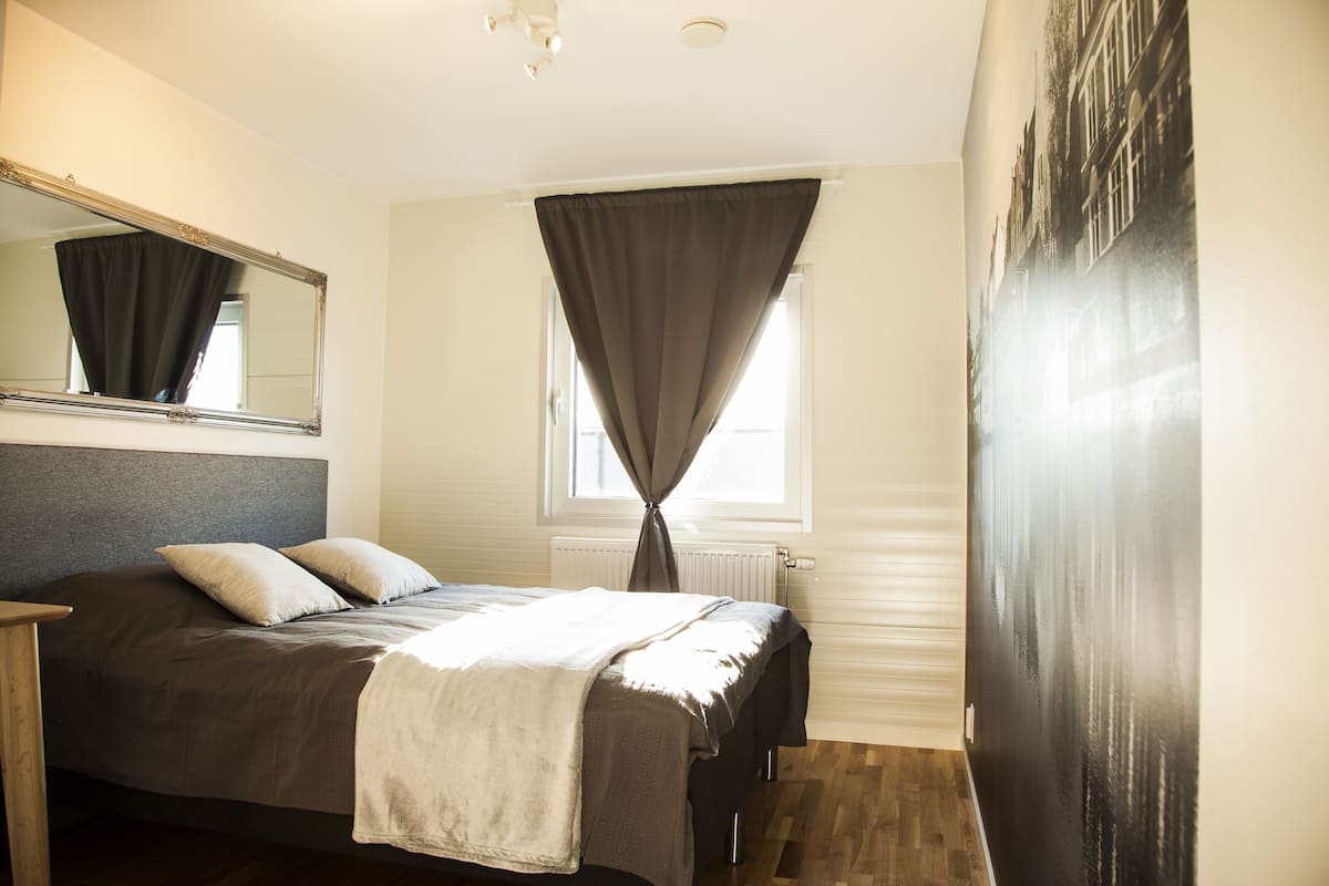 Un dormitorio con cama, un espejo grande, una ventana con cortinas y un radiador.