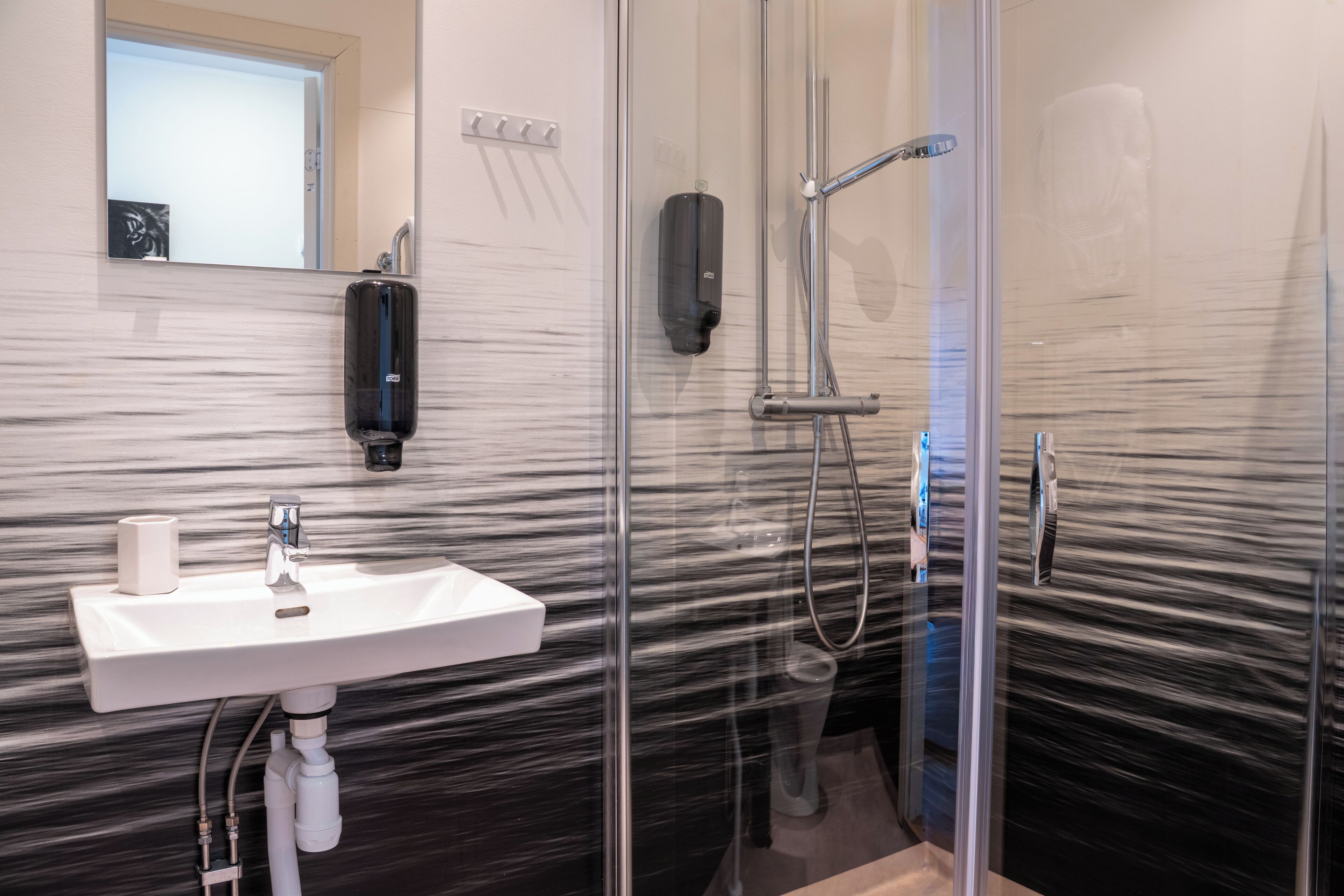 Un baño moderno con cabina de ducha de vidrio, un lavamanos blanco y dispensador de jabón para manos.
