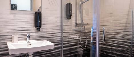 Un baño moderno con cabina de ducha de vidrio, un lavamanos blanco y dispensador de jabón para manos.