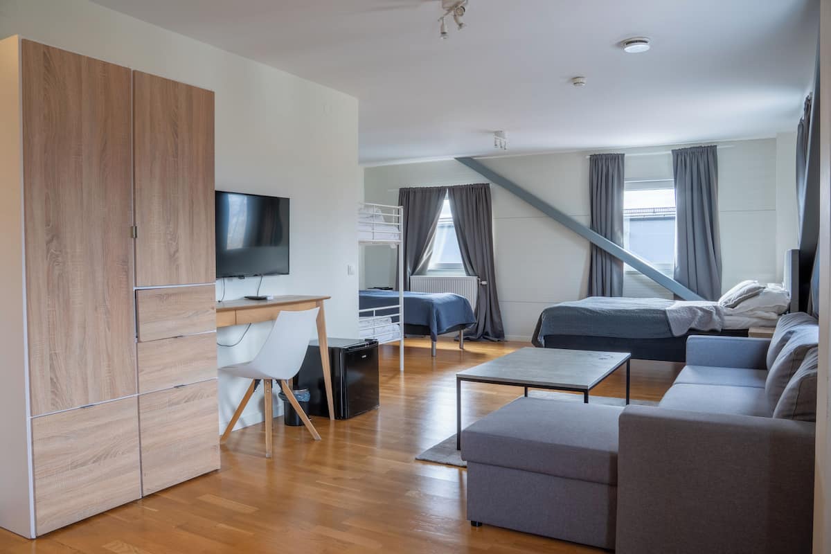 Una habitación moderna con un armario de madera, un escritorio con ordenador, una cama, un sofá y un televisor.
