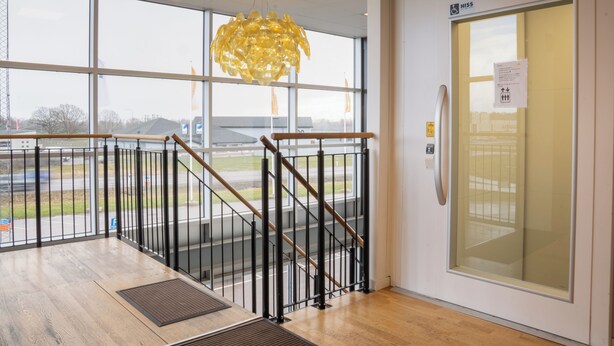 A modern interior with a staircase, large windows, and a glass door with an accessibility sign. - Hotell Tunapark (Eskilstuna)