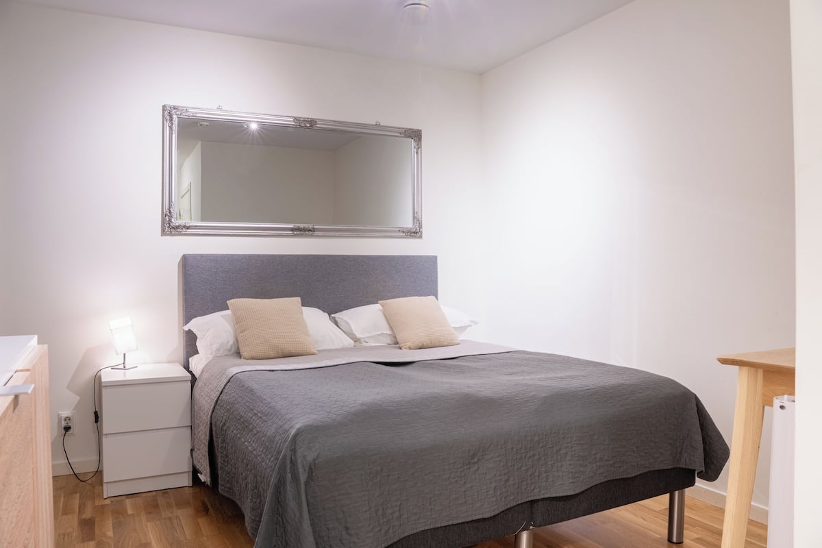 Un dormitorio con cama, mesita de noche y espejo en la pared.