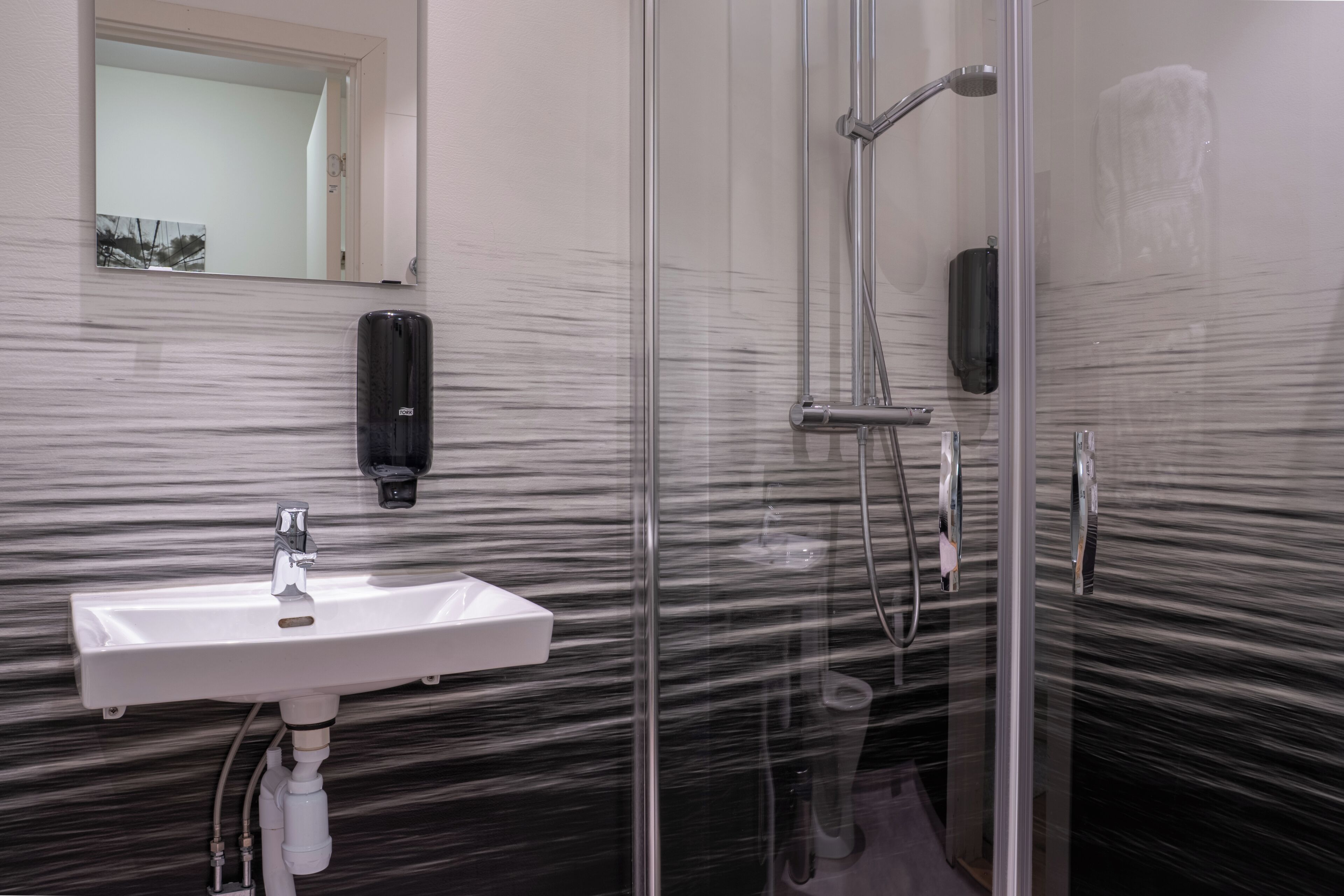 Un baño con cabina de ducha de vidrio, un lavabo blanco y un dispensador de gel antibacterial.