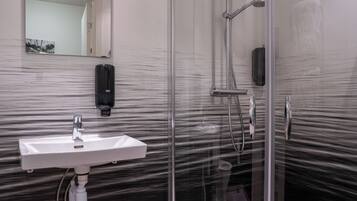 Un baño con cabina de ducha de vidrio, un lavabo blanco y un dispensador de gel antibacterial.