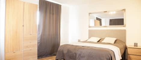 Un dormitorio con cama, armario, espejo y mesita de noche.