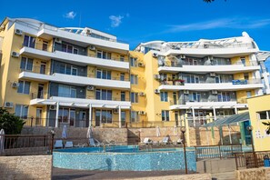 Un hotel de varios pisos con balcones, una piscina y un cielo azul despejado.