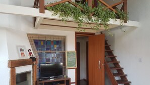 A compact living space with a wooden staircase, a TV on a glass cabinet, and a hanging plant. - Solar das Pétalas (Florianópolis)